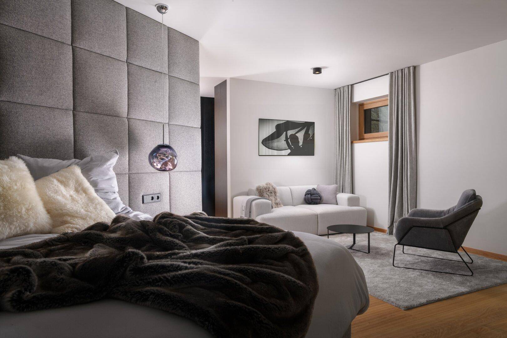 Gemütliches Schlafzimmer mit gepolsterter Wand, weichen Textilien und Sitzbereich.
