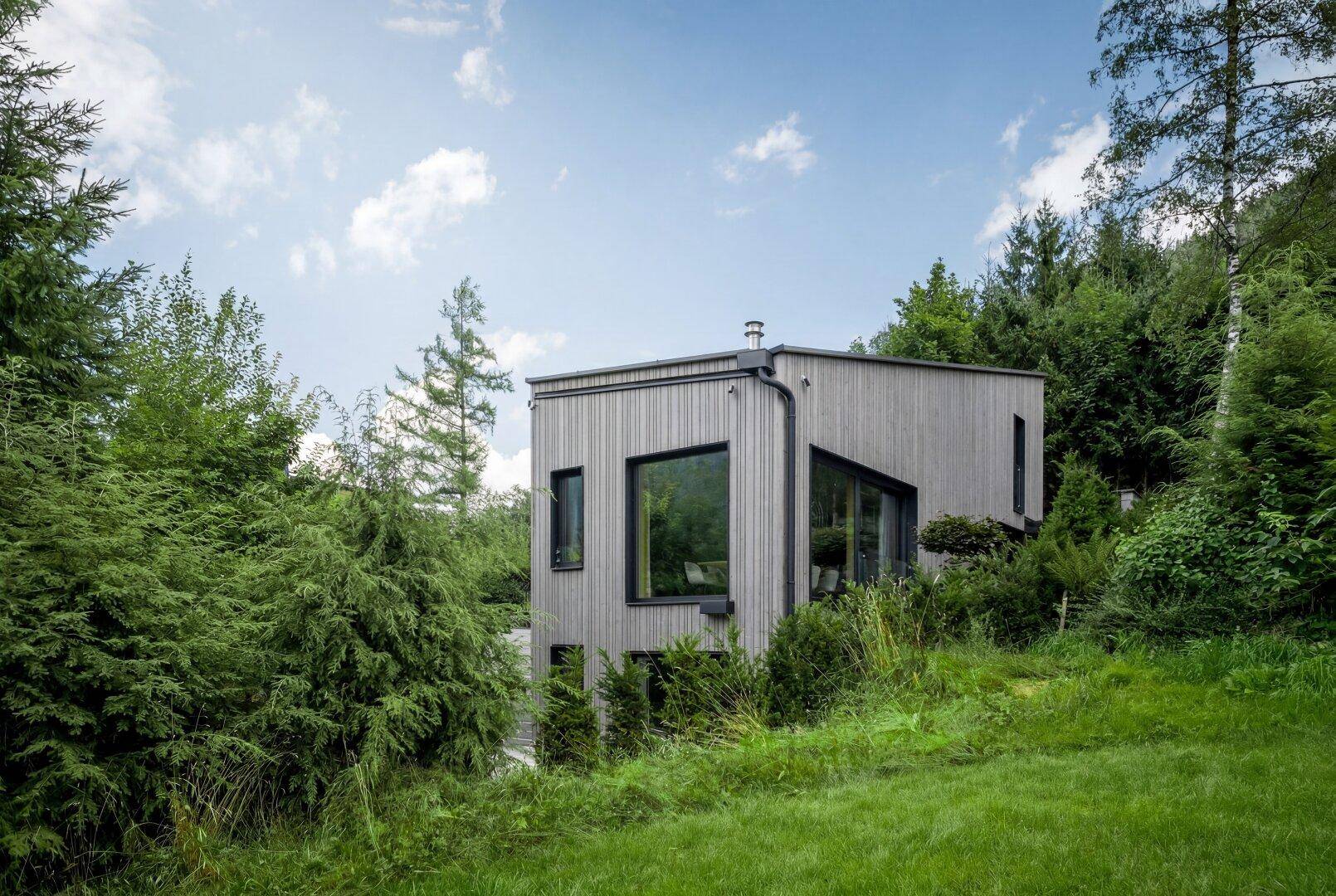 Modernes Holzhaus in grüner, bewaldeter Umgebung mit viel Natur.