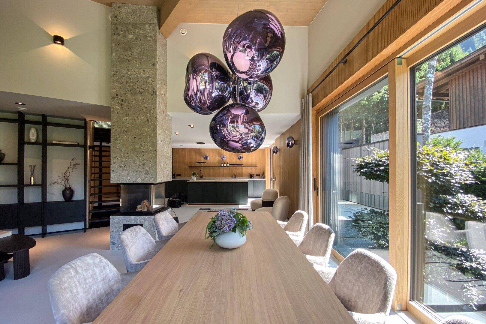 Eleganter Essbereich mit großem Holztisch, Designerlampen und Blick ins Grüne.