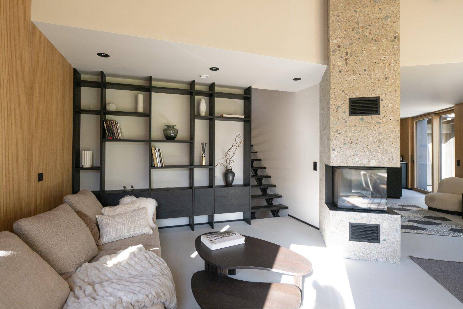 Modernes Wohnzimmer mit integriertem Bücherregal, Kamin und Zugang zu einer Treppe.