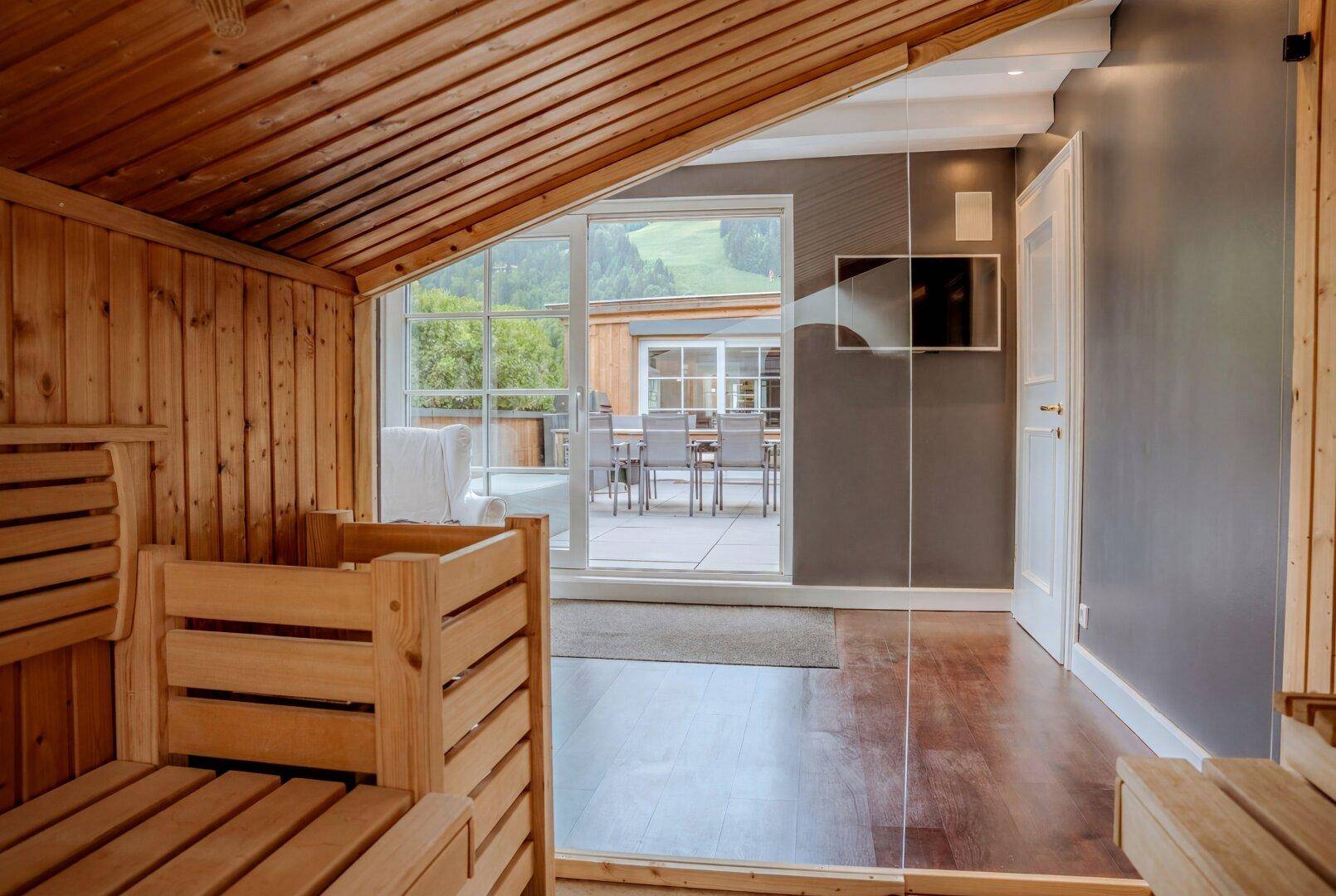 Gemütliche Holzsauna mit Blick auf die Terrasse und die grüne Berglandschaft durch die Glasschiebetür.