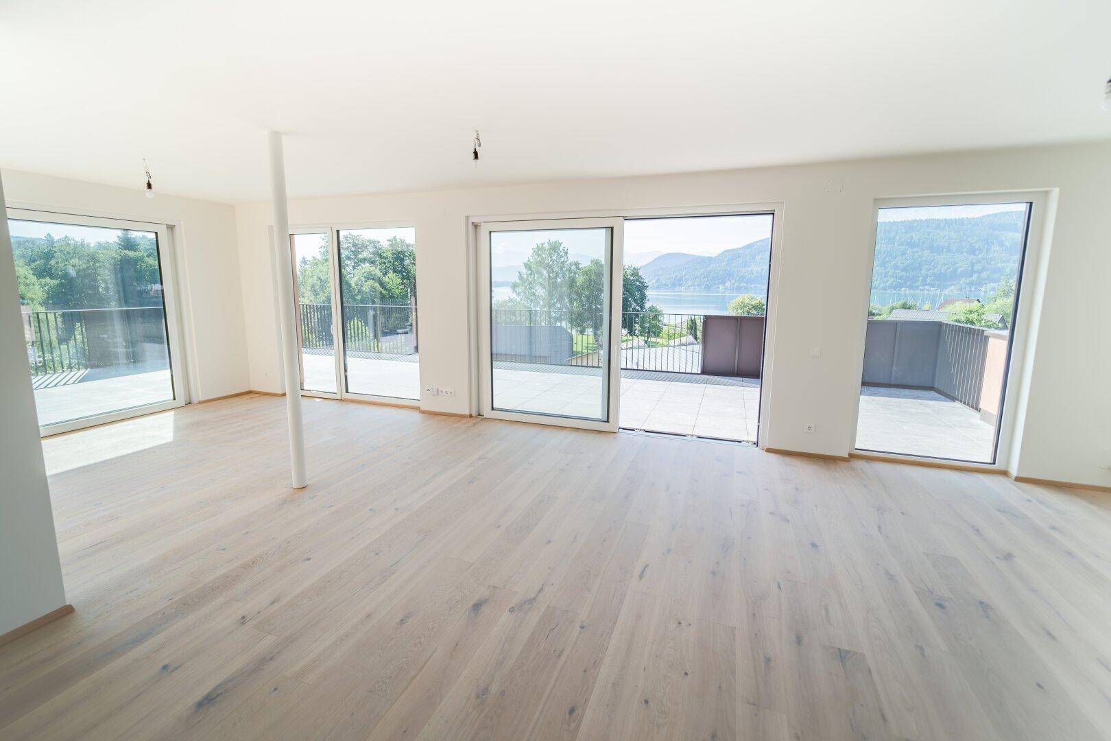 Helles, leeres Wohnzimmer mit Holzboden und großen Schiebetüren zur Terrasse mit Seeblick.