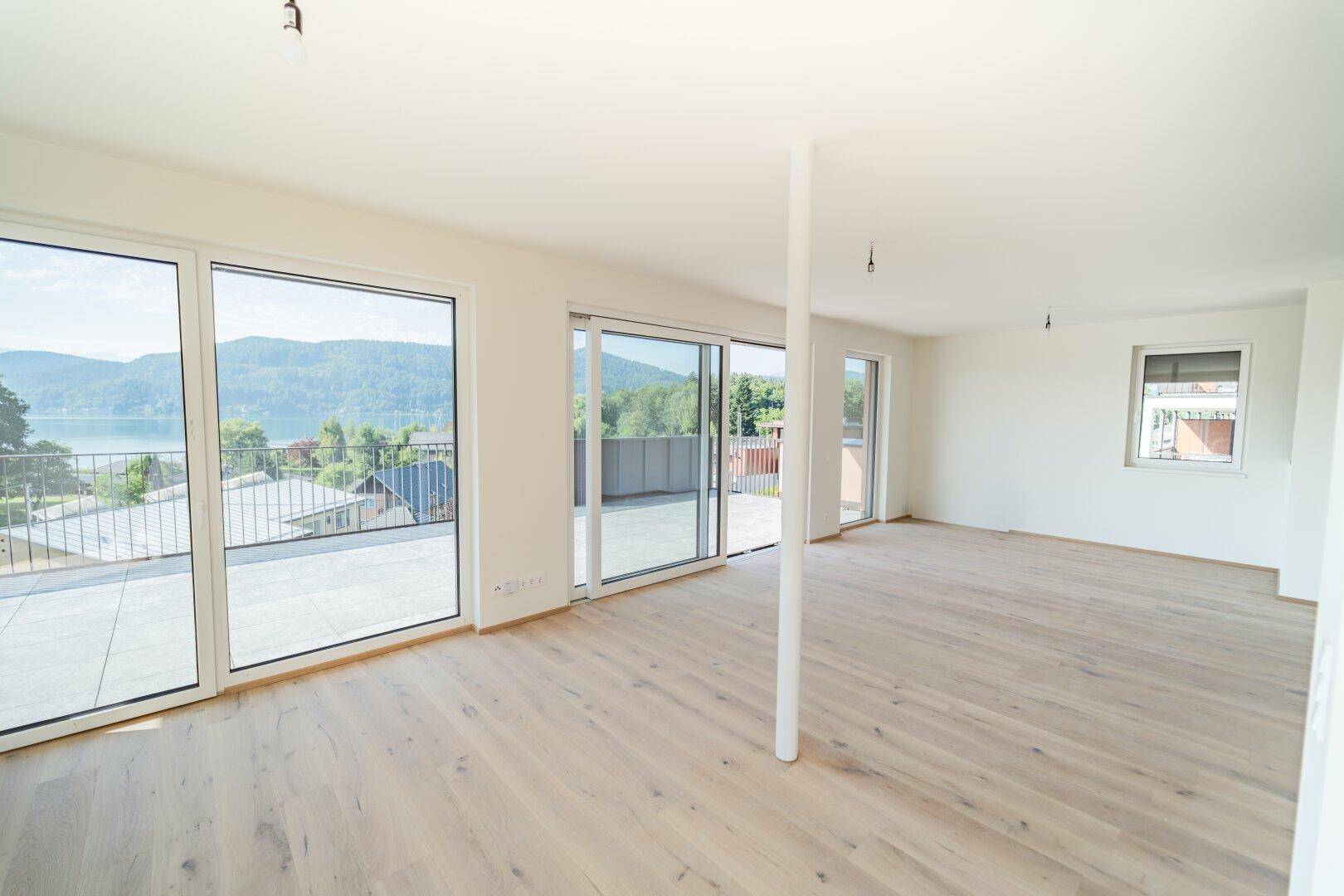 Geräumiges, helles Wohnzimmer mit Holzboden und weitem Blick auf den See und die Berge.