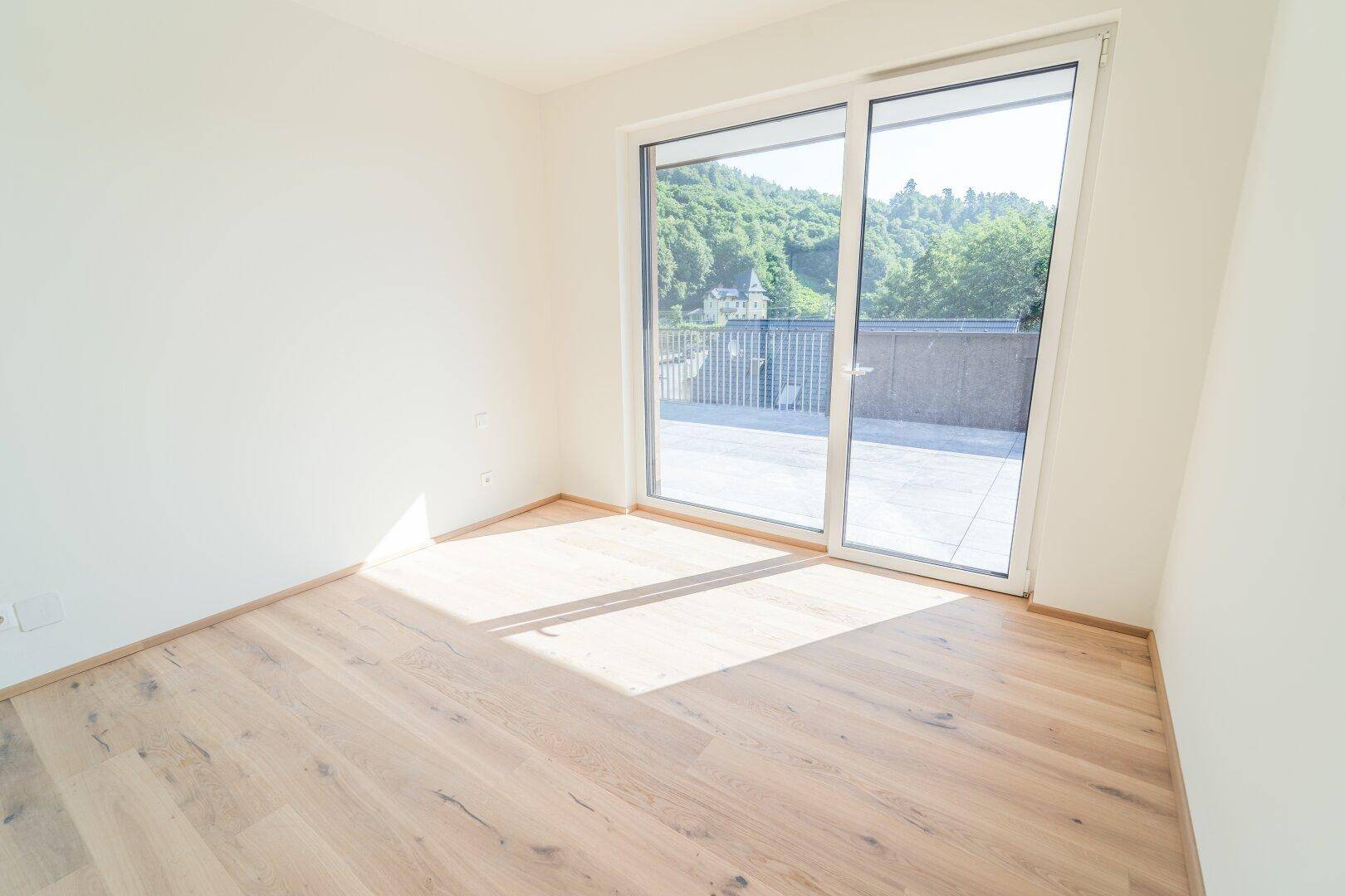 Helles Schlafzimmer mit Holzboden und direktem Zugang zur sonnigen Terrasse mit Bergblick.