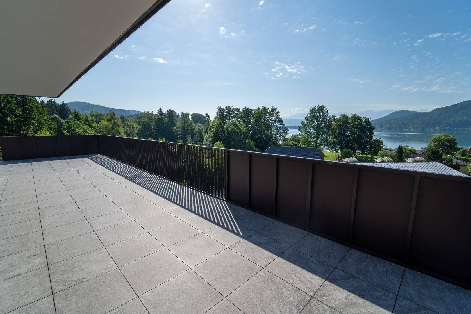 Geräumige, geflieste Terrasse mit moderner Brüstung und weitem Blick auf den See und die Umgebung.