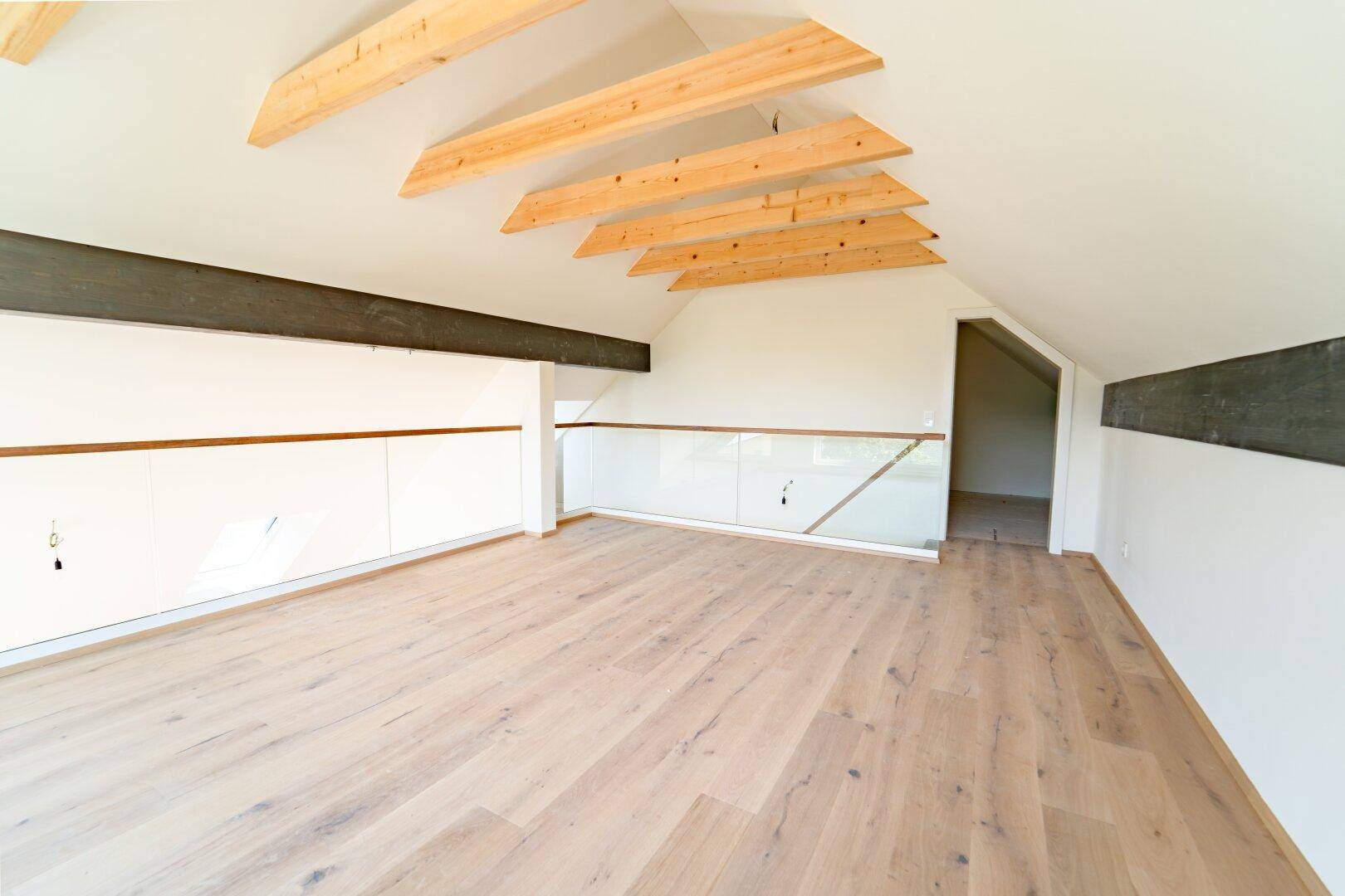 Offene Galerie mit Holzboden, sichtbaren Holzbalken und integrierten Stauschränken unter der Dachschräge.