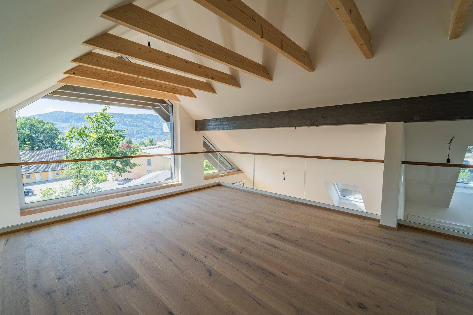 Helle Galerieebene mit Holzboden, sichtbaren Holzbalken und weitem Blick auf die Landschaft.