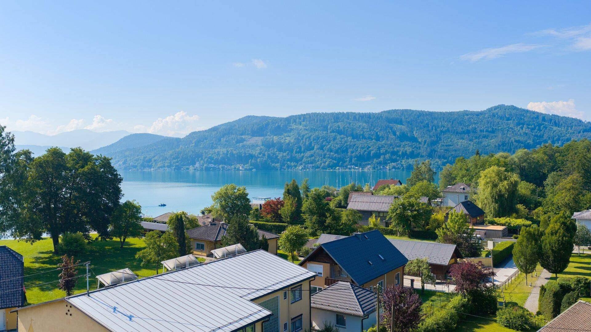 Panoramablick auf einen ruhigen See, umrahmt von bewaldeten Hügeln und einer malerischen Siedlung.