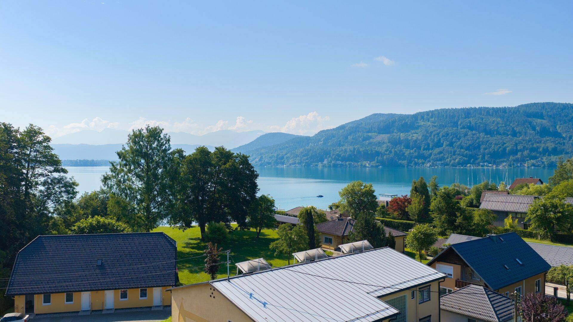 Weitläufiger Blick über die Häuser auf den glitzernden See und die bewaldeten Berge am Horizont.