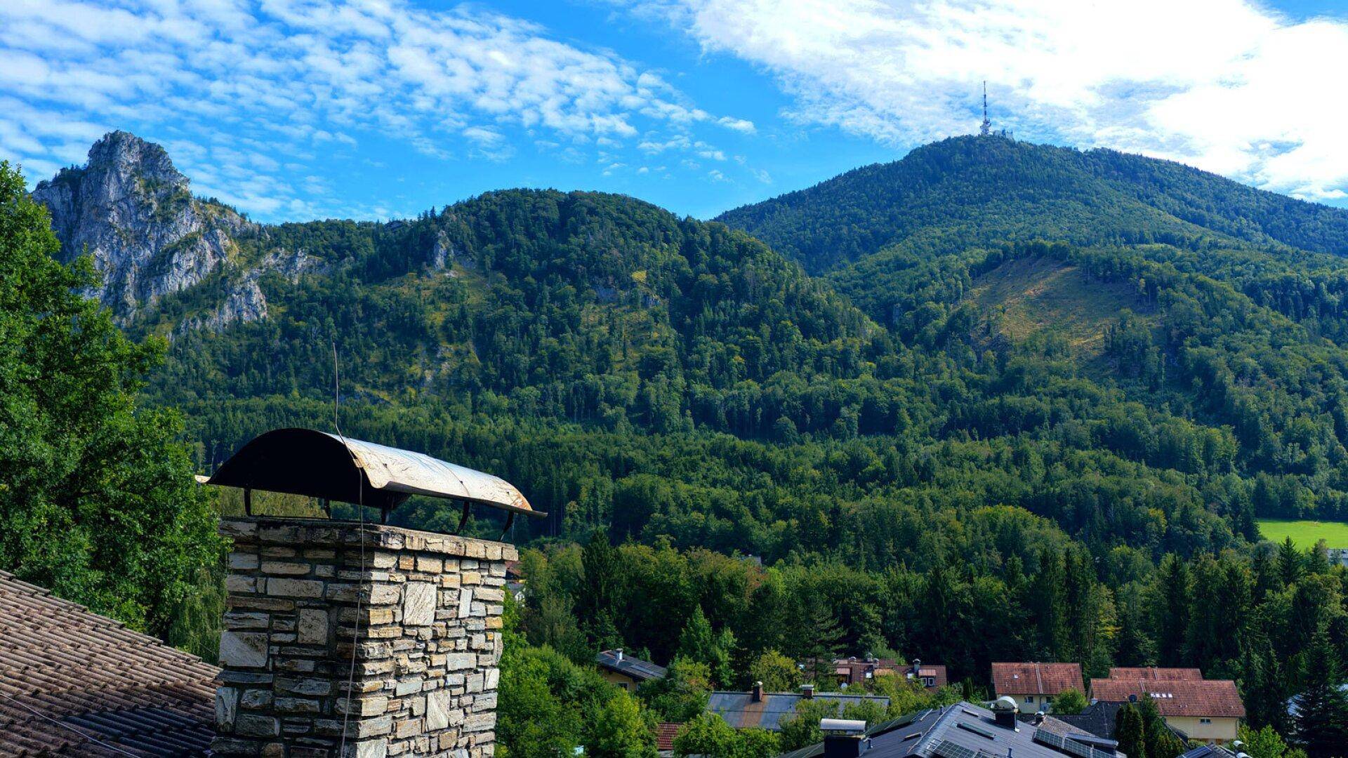 Weitläufiger Blick auf bewaldete Berge unter blauem Himmel, mit einem steinernen Schornstein im Vordergrund.