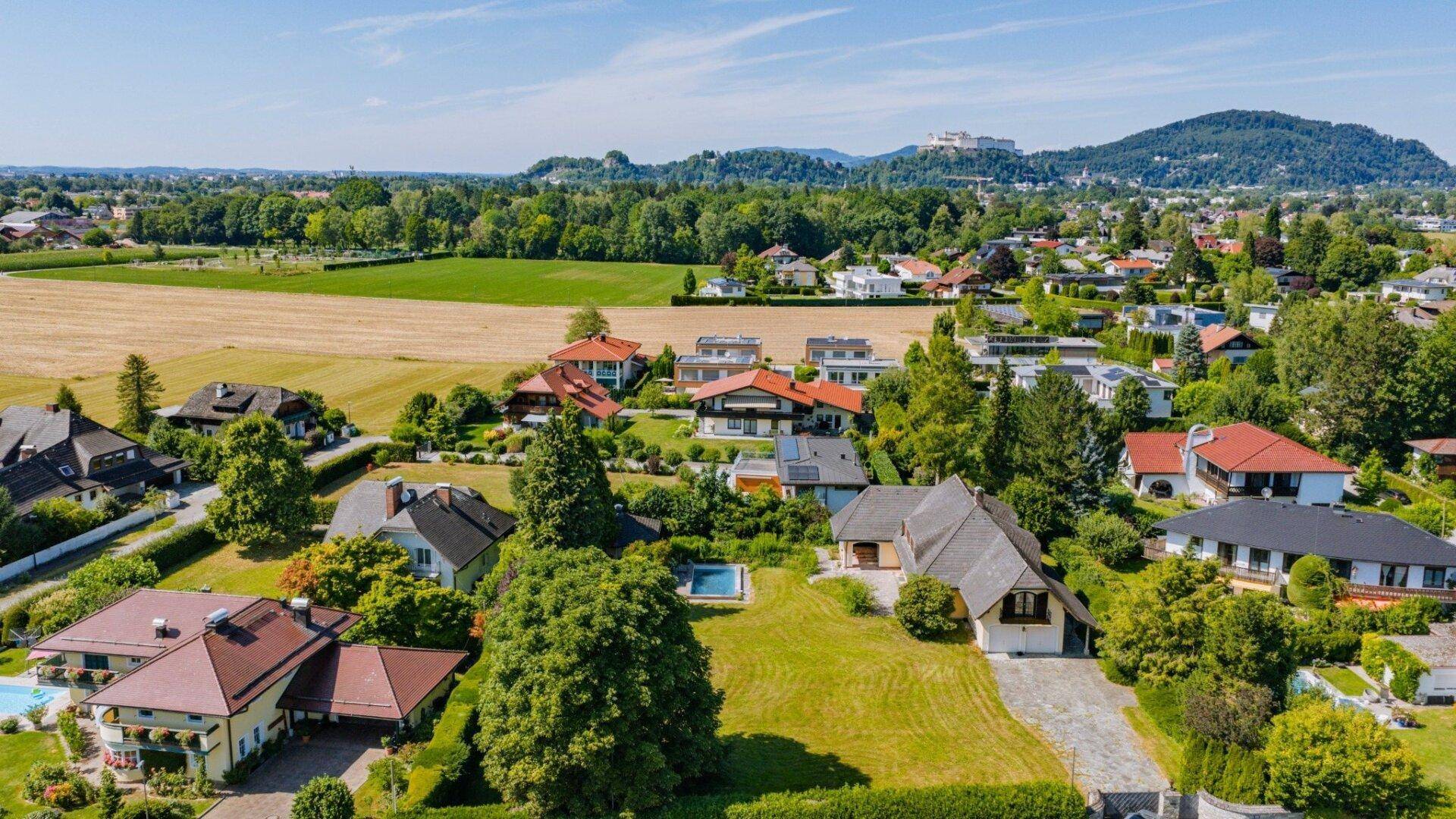 Luftaufnahme einer Wohnsiedlung mit gepflegten Gärten, einigen Pools und einem weiten Blick auf die umliegende Landschaft.