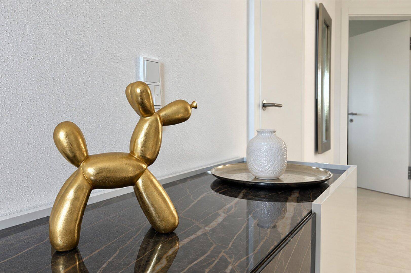 Dekoratives goldenes Ballonhund-Objekt auf einem eleganten Sideboard in einem hellen Flur.