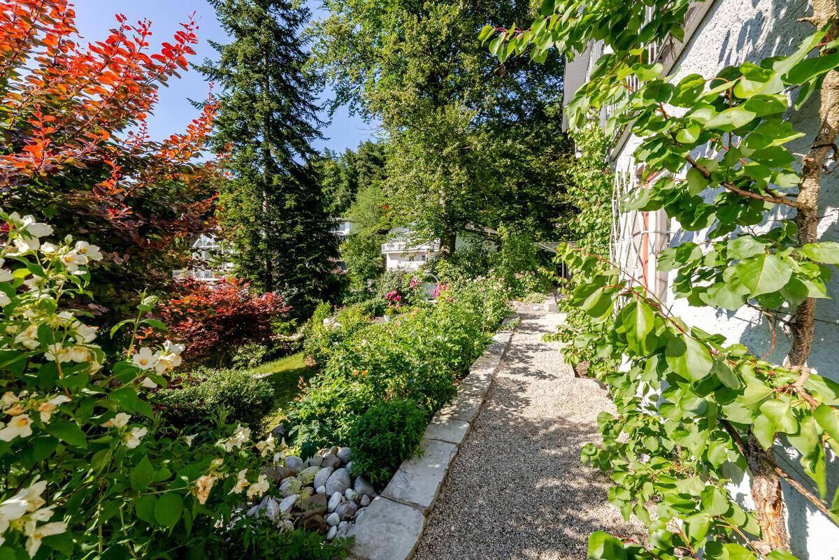 Kiesweg im Garten, gesäumt von üppiger Bepflanzung und Blumen, entlang der Hauswand.