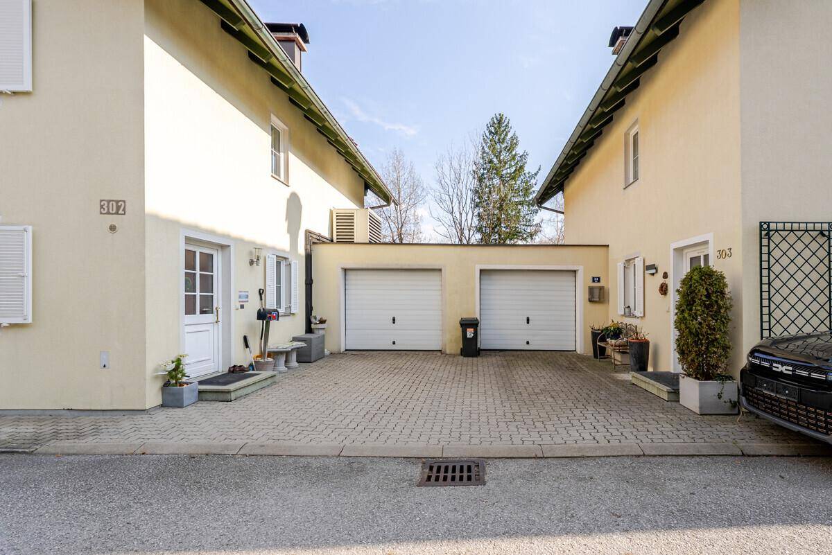 Doppelgarage mit gepflasterter Zufahrt zwischen zwei Wohnhäusern.