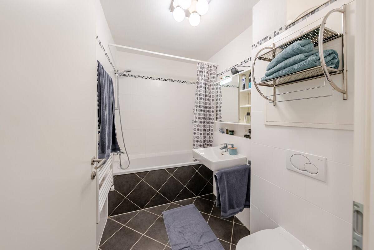 Badezimmer mit Badewanne, Duschvorhang, WC und dunklen Bodenfliesen.