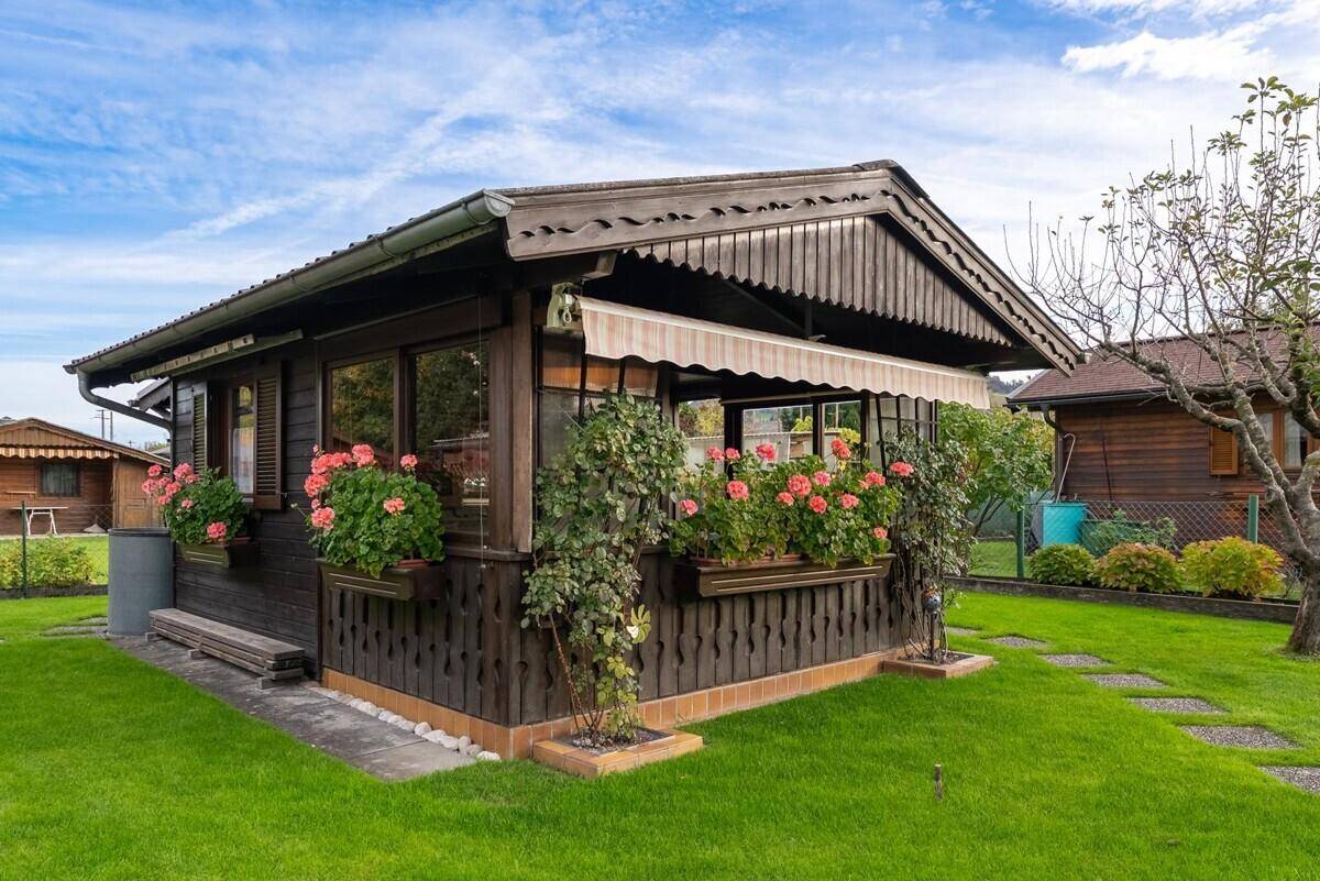Charmantes Holzhaus mit Blumenkästen, Markise und gepflegtem Rasen im Vordergrund.