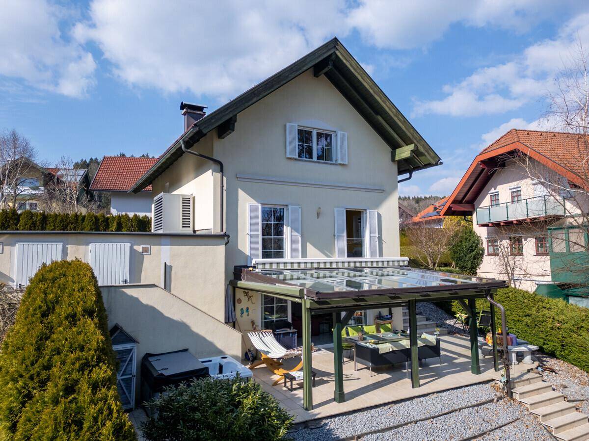 Rückansicht des Hauses mit Wintergarten, Terrasse und Gartenbereich unter blauem Himmel.