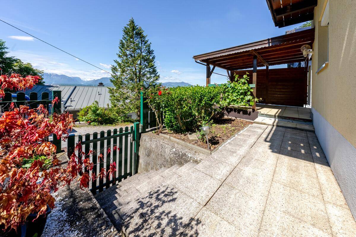 Gepflasterter Weg führt durch den Garten zu einem überdachten Sitzbereich mit Bergblick.