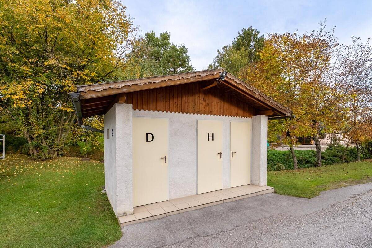Kleines Nebengebäude mit zwei Türen, wahrscheinlich für sanitäre Anlagen, umgeben von Bäumen.