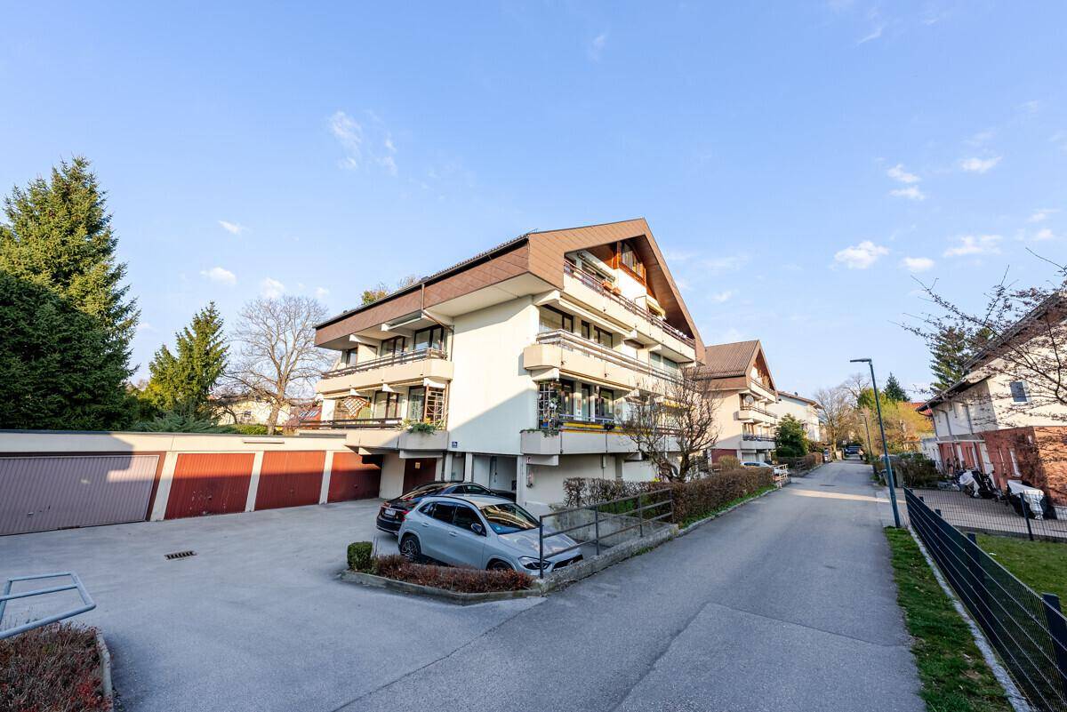 Mehrfamilienhaus mit Satteldach, Parkplätzen und einer Rampe für barrierefreien Zugang.