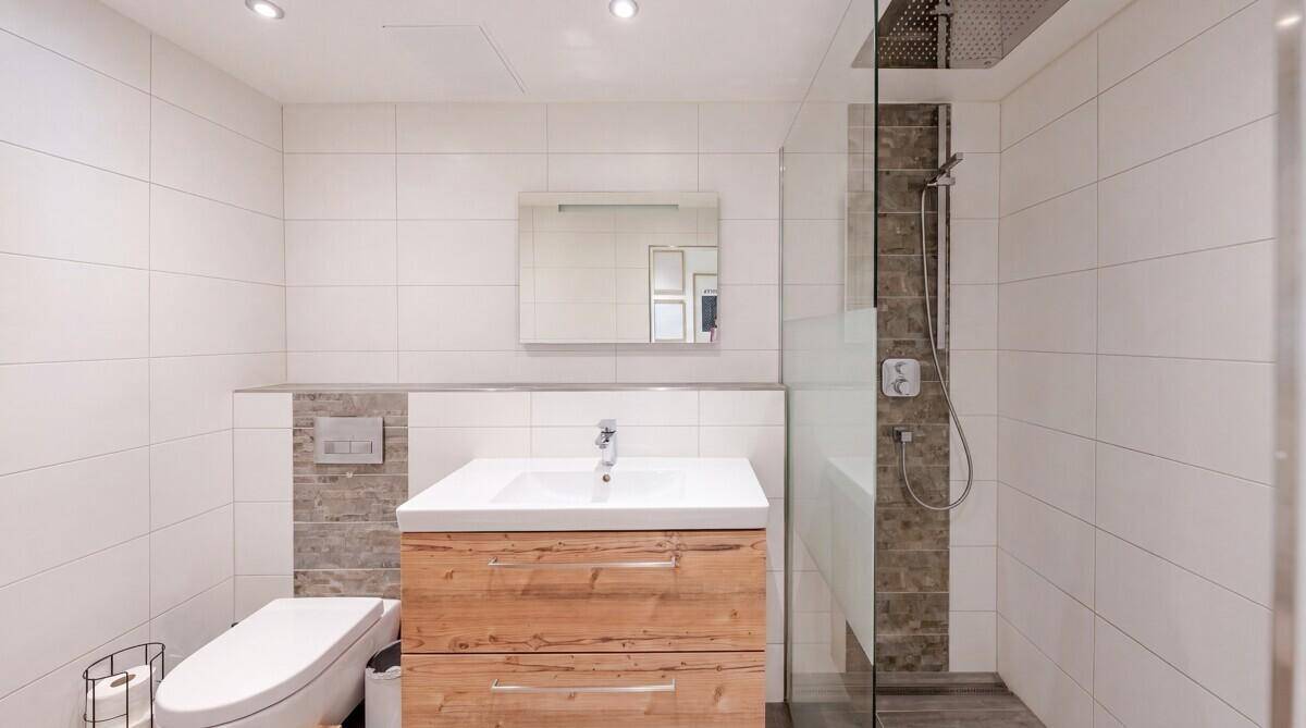 Modernes Badezimmer mit weißen Fliesen, Holzwaschtisch und einer geräumigen begehbaren Dusche.