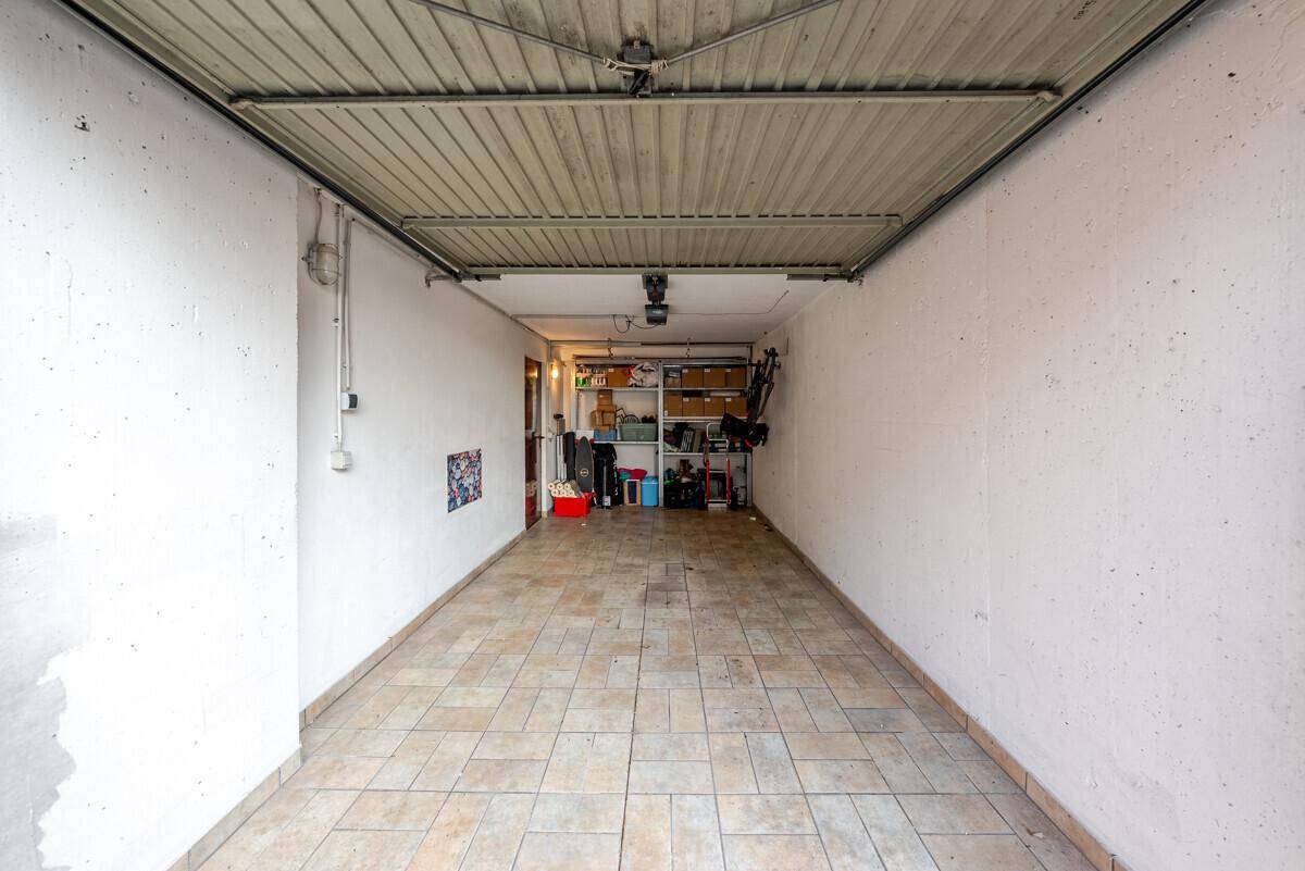 Leere Garage mit Fliesenboden und praktischen Regalen für zusätzlichen Stauraum.