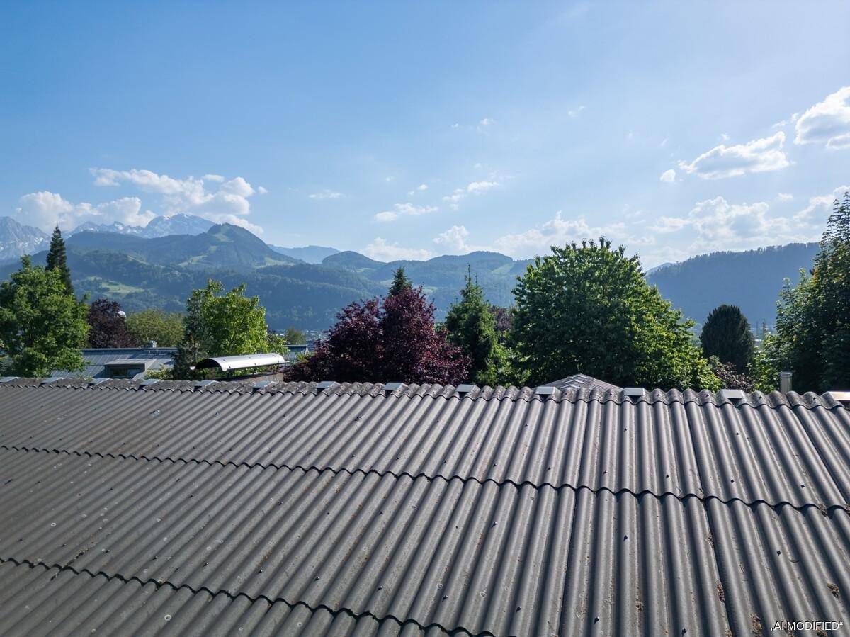 Weitblick über ein Wellblechdach auf eine malerische Berglandschaft und grüne Bäume.