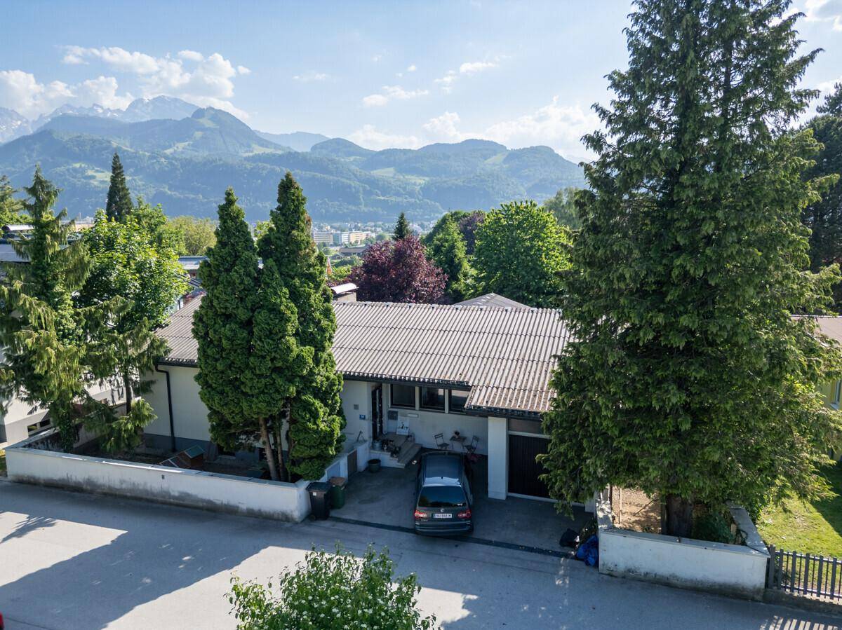 Einfamilienhaus mit Garten und Bergblick, umgeben von Bäumen und einer ruhigen Straße.
