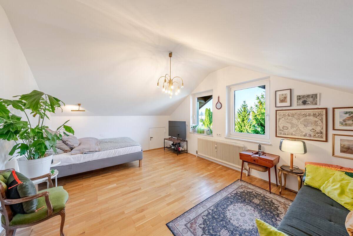 Geräumiges Dachzimmer mit Holzboden, schrägen Wänden und viel natürlichem Licht.