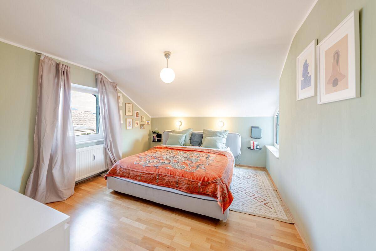 Schlafzimmer im Dachgeschoss mit schrägen Wänden, Holzboden und gemütlichem Bett.