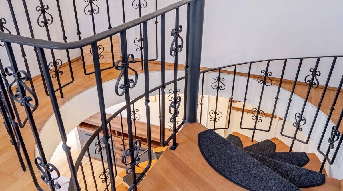 Elegante Wendeltreppe mit schmiedeeisernem Geländer und Holzstufen, die die Etagen verbindet.