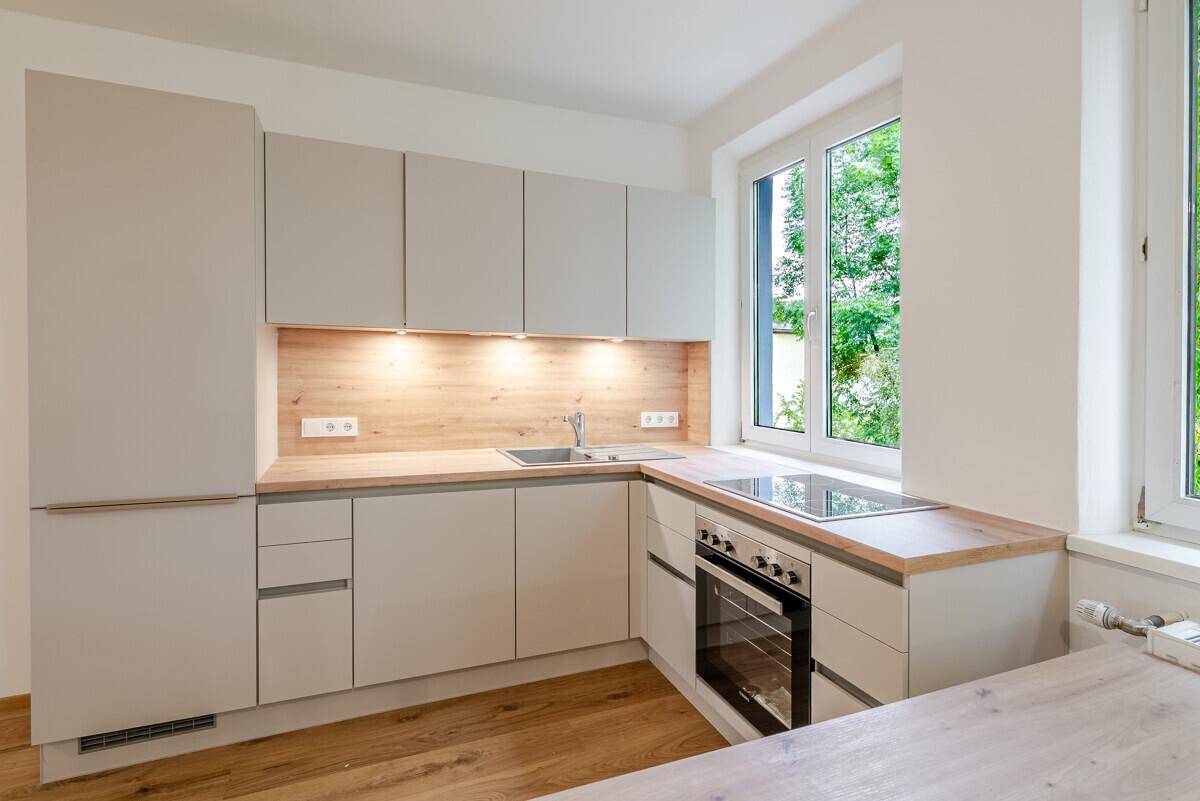 Moderne Einbauküche mit hellen Schränken, Holzarbeitsplatte und Fenster mit Blick ins Grüne.