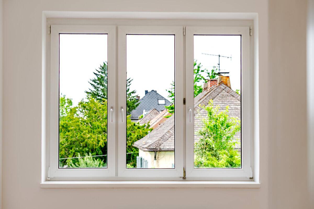 Fenster mit Blick auf die Dächer der Nachbarhäuser und üppiges Grün der Bäume.