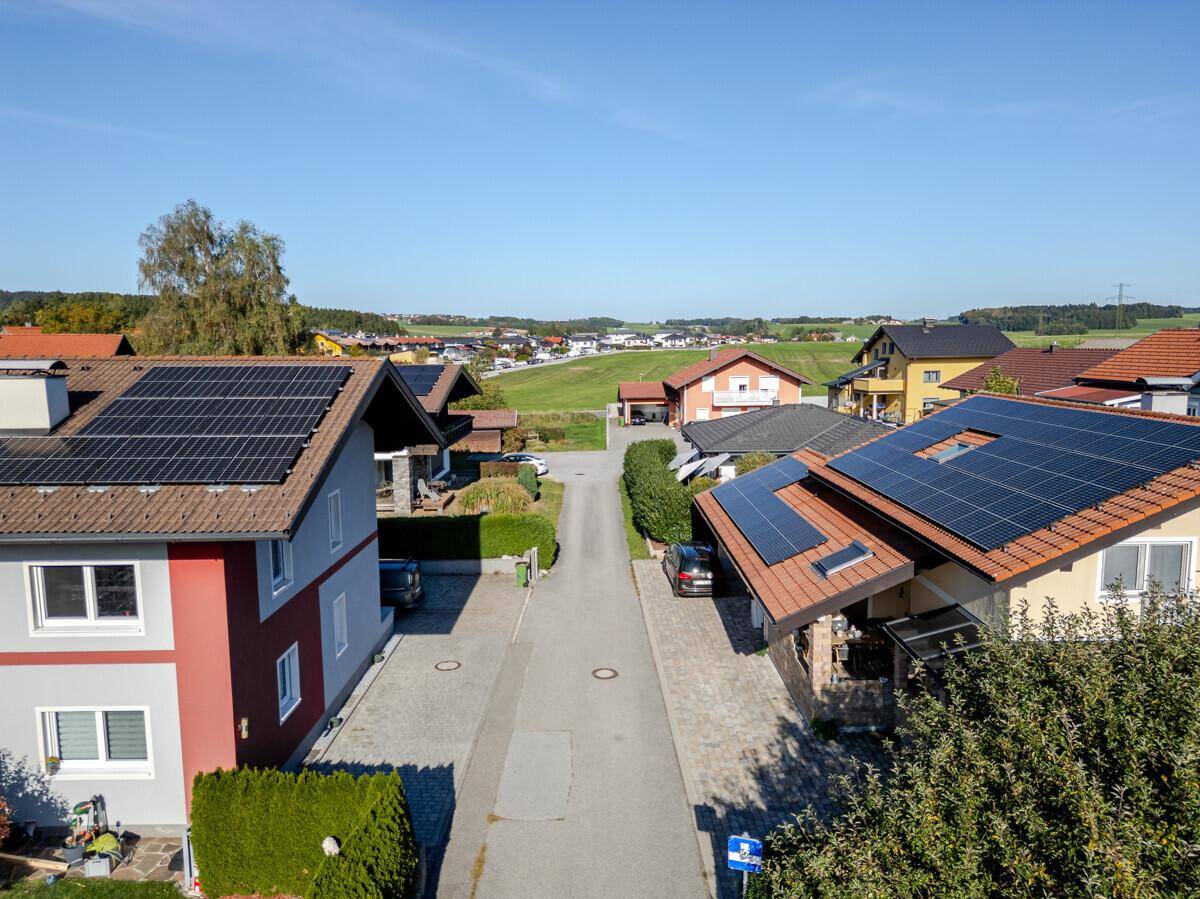 Luftaufnahme einer Wohnstraße mit Häusern, Solaranlagen und weitem Blick auf die ländliche Umgebung.
