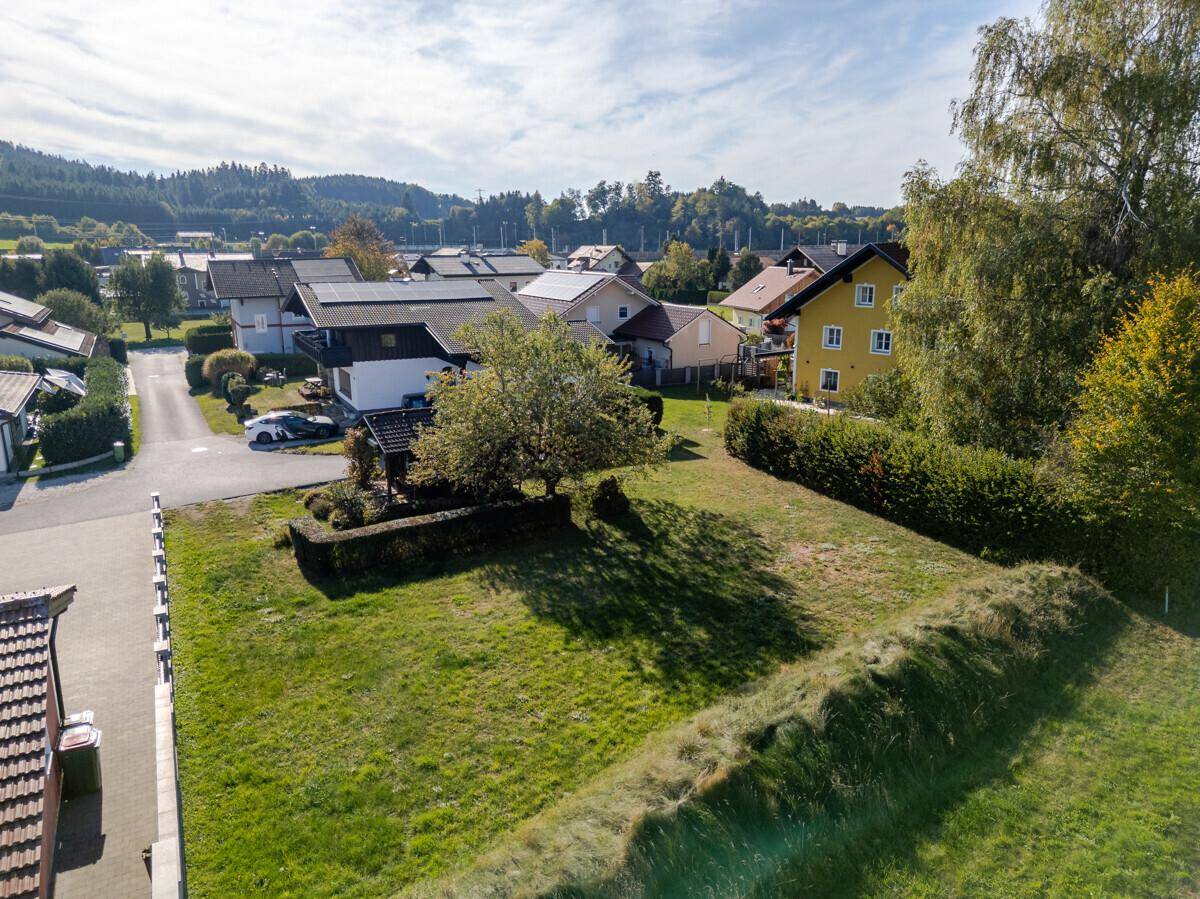 Luftaufnahme eines unbebauten Grundstücks in einer Wohngegend mit umliegenden Häusern und Bergen.