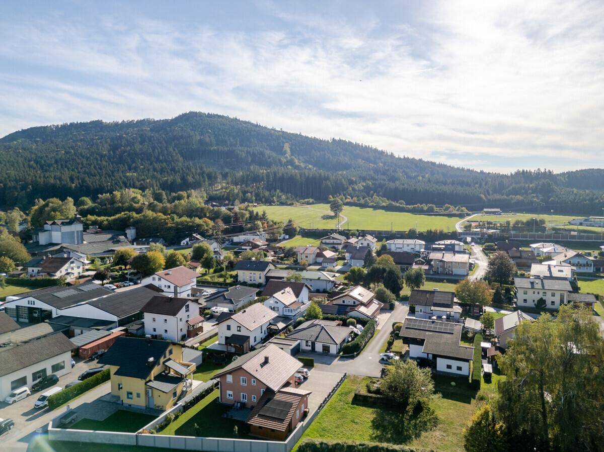 Luftaufnahme eines Wohn- und Gewerbegebiets mit Häusern, Gebäuden und bewaldetem Berg im Hintergrund.