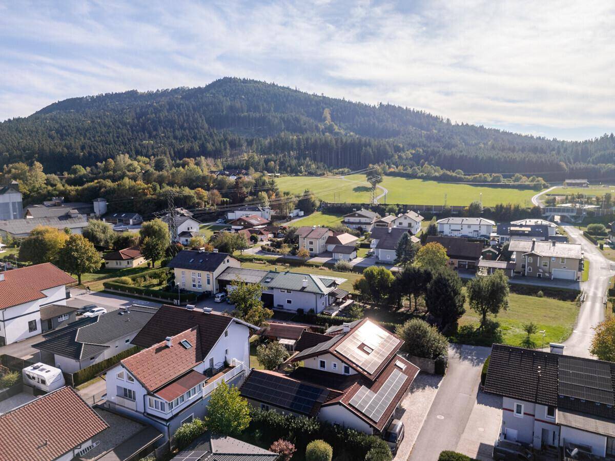 Luftaufnahme einer Wohnsiedlung mit Häusern, Solaranlagen und einem bewaldeten Berg im Hintergrund.