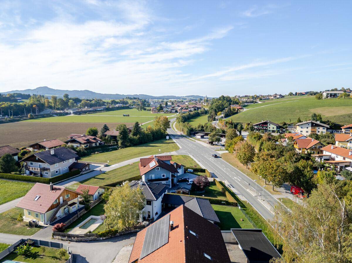 Luftaufnahme einer Straße, die durch ein Wohngebiet mit Häusern und grünen Feldern führt.