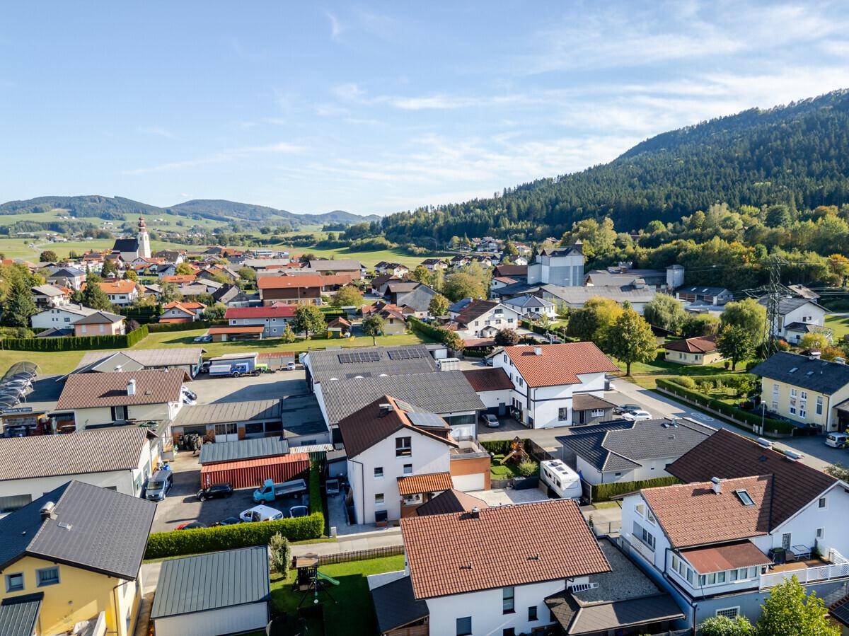 Luftaufnahme eines Wohn- und Gewerbegebiets mit Häusern, Gebäuden und bewaldetem Berg im Hintergrund.