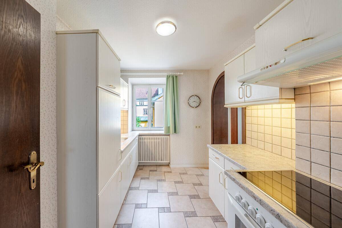 Helle Küche mit weißen Schränken, Fliesenboden und einem Fenster mit Blick nach draußen.