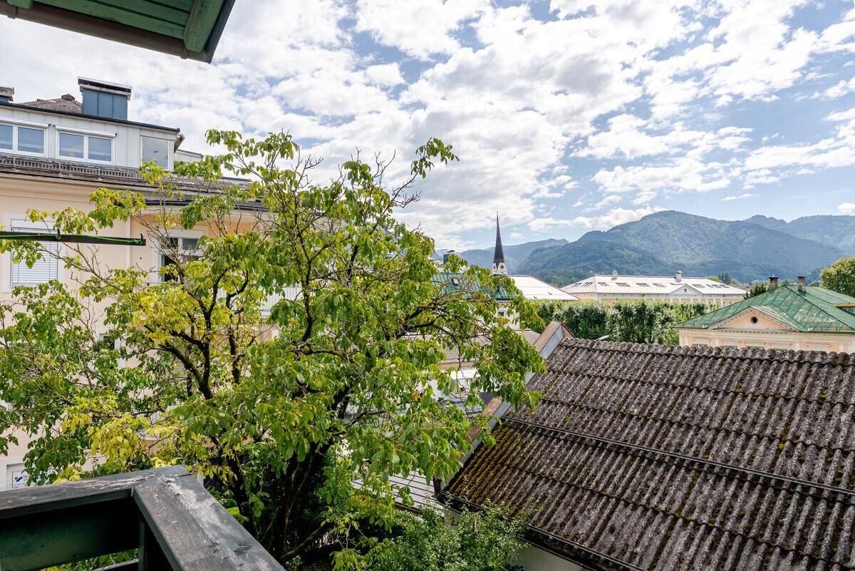 Weitblick vom Balkon über grüne Bäume und die Dächer der Stadt bis zu den Bergen.
