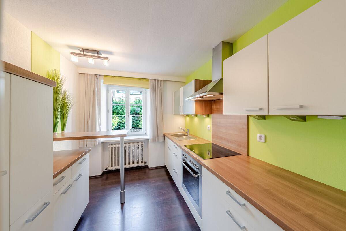 Funktionale Küche mit weißen Schränken, Holztheke und einem Fenster mit Gartenblick.