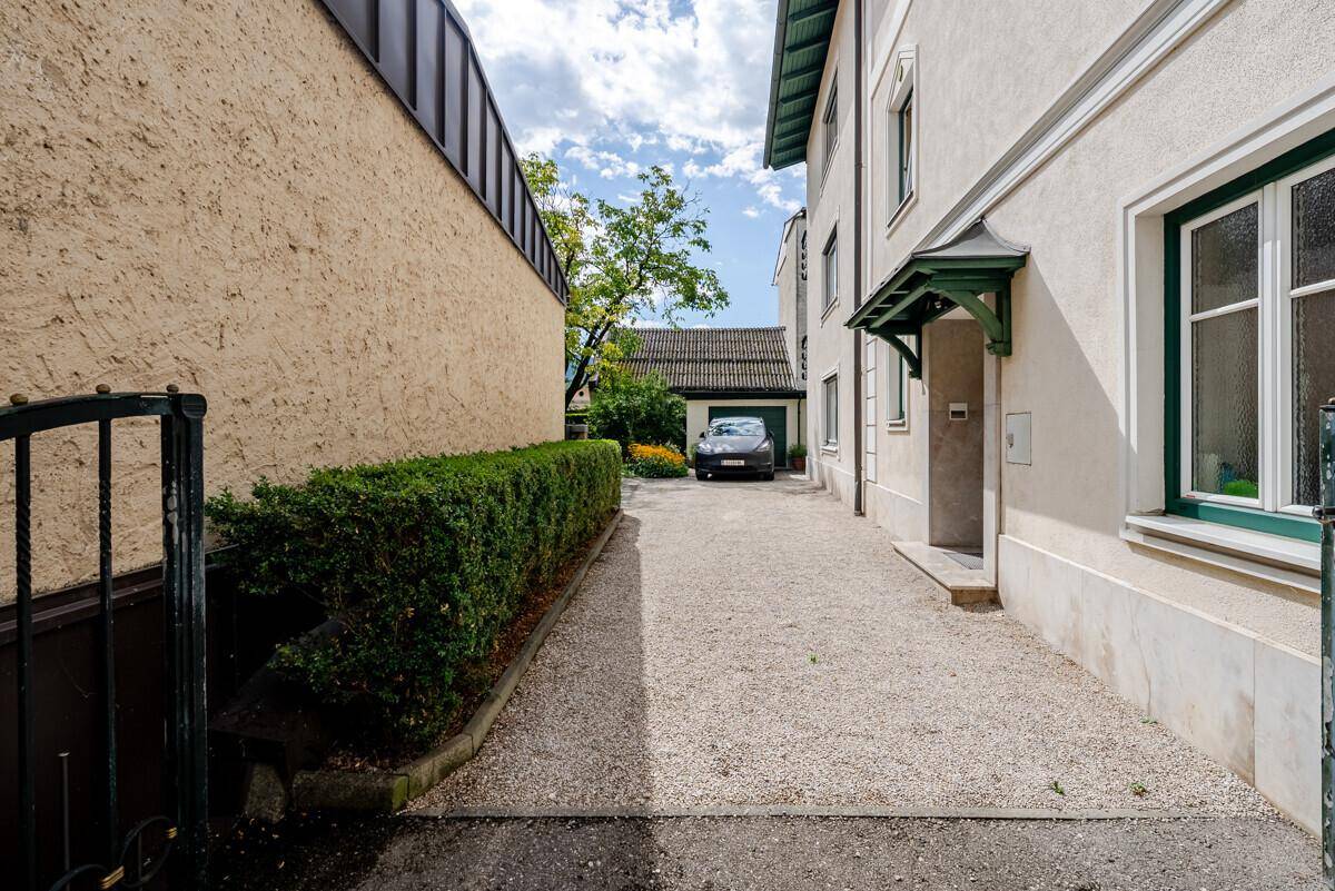 Kiesauffahrt zum Eingangsbereich des Gebäudes mit gepflegter Hecke und Parkplatz.