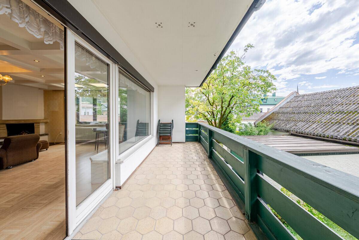 Langer Balkon mit Fliesenboden und grüner Holzbrüstung, zugänglich vom Wohnbereich.