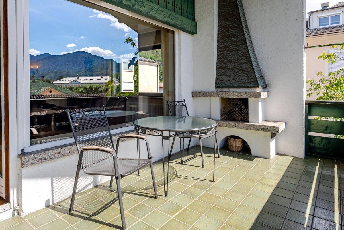 Sonniger Balkon mit Außenkamin, Sitzgelegenheiten und Panoramablick auf die Berge.