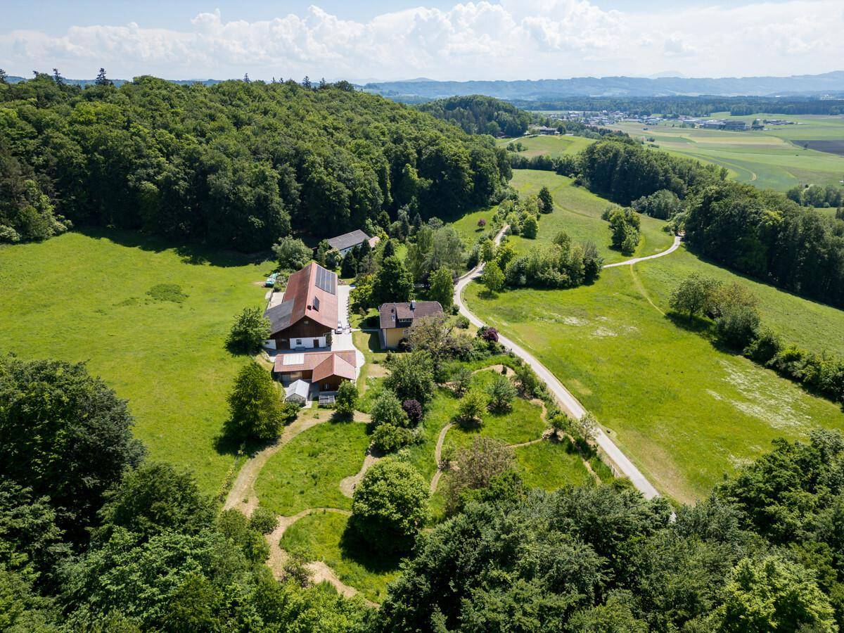 Weitläufige Luftaufnahme des Anwesens, eingebettet in eine grüne Hügellandschaft mit Wäldern und Feldern.