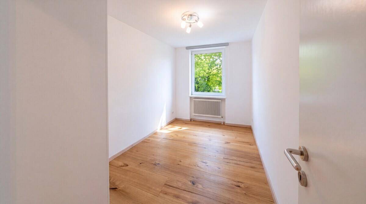 Helles Zimmer mit Holzboden und einem Fenster, das viel Tageslicht hereinlässt.