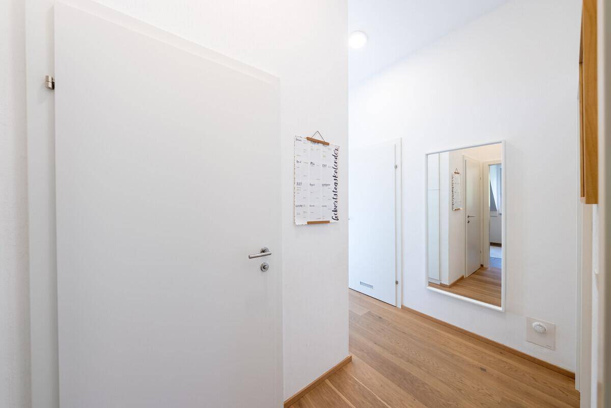 Heller Flur mit Holzboden und einem Spiegel, der den Raum optisch erweitert.