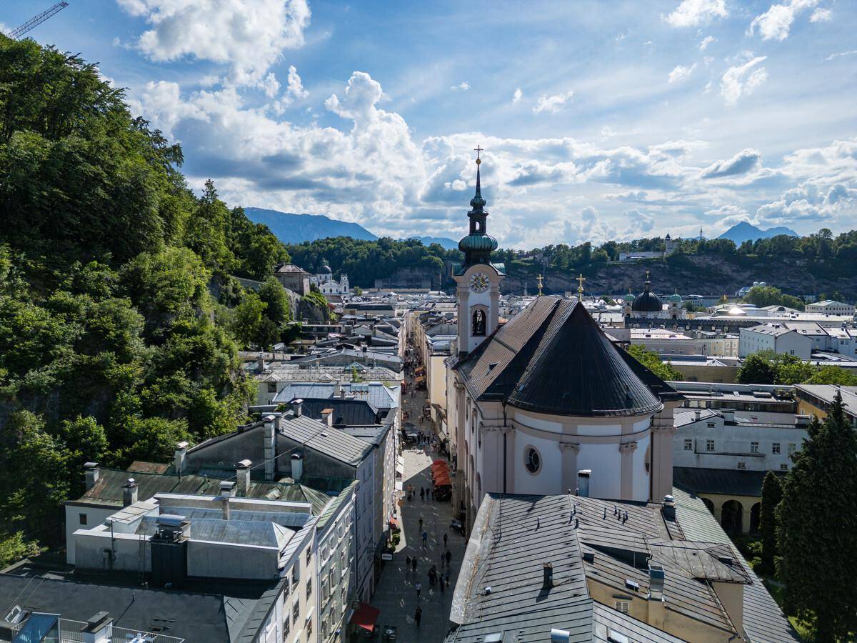 Panoramablick auf eine historische Stadt mit einer markanten Kirche, umgeben von Gebäuden und grünen Hügeln.