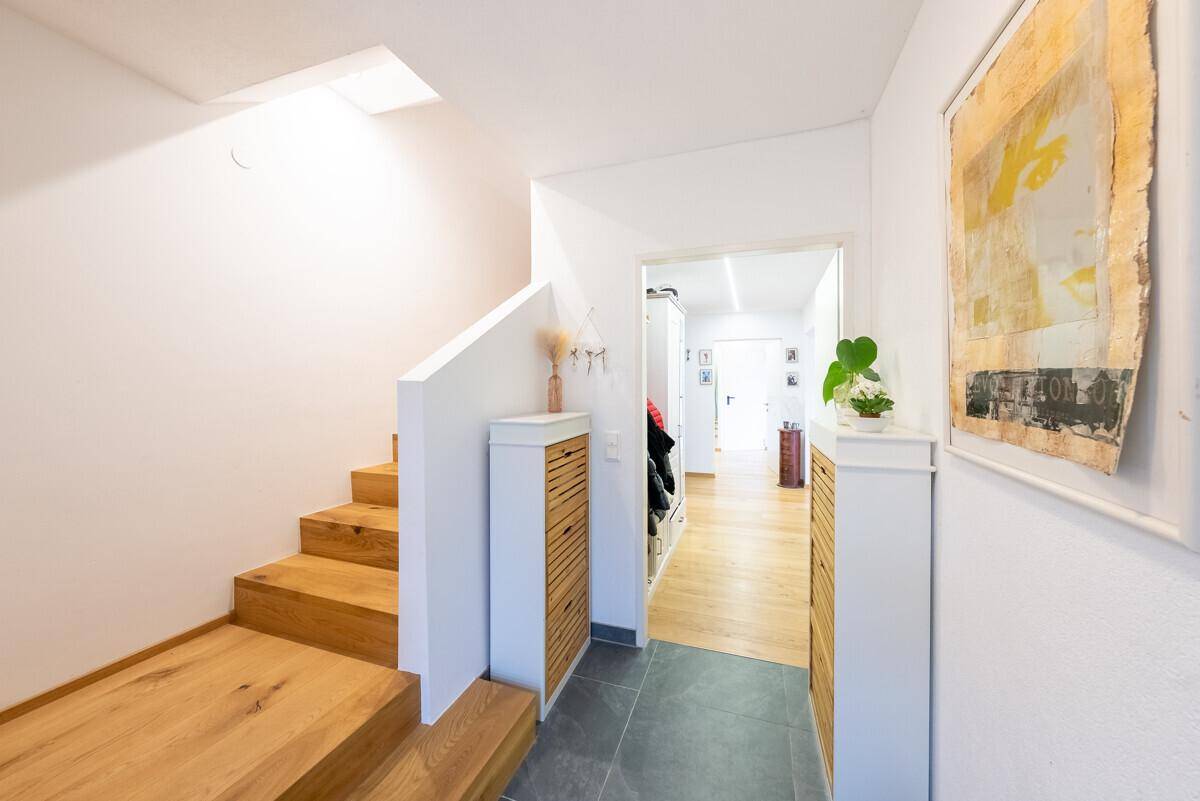 Heller Flur mit Holztreppe und Fliesenboden, der zu den oberen Etagen führt.